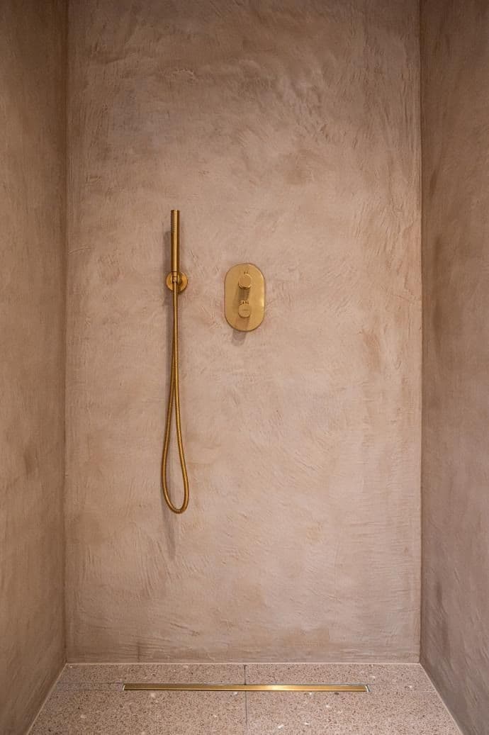 a bathroom with a gold shower head in the corner and a towel rack on the wall, classique, tadelakt