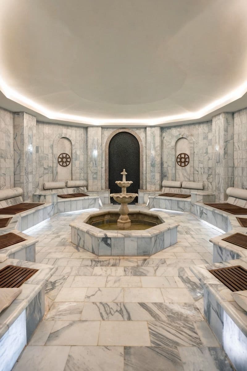 a room with benches and a fountain in the center, surrounded by white marble walls, classique, marbre
