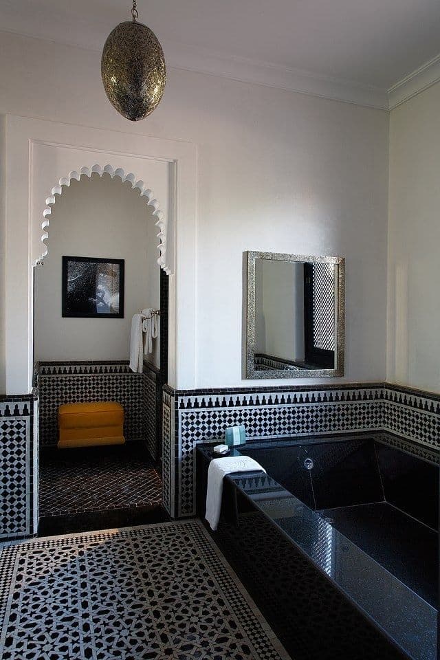 an ornate bathroom with black and white tiles on the floor, walls and bathtub, classique, zellige